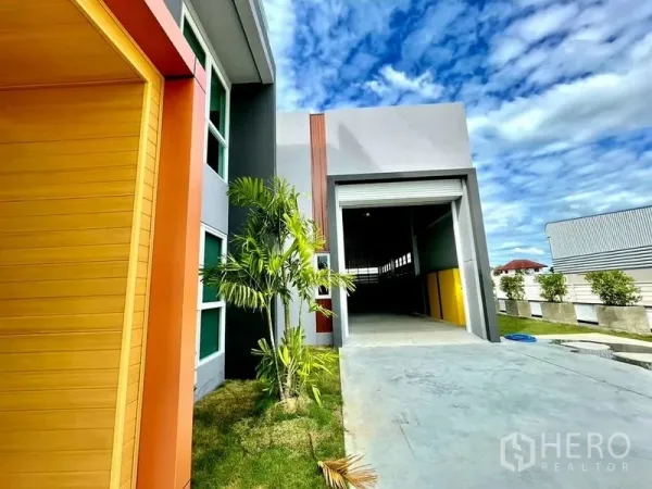 Warehouse for sale in Lam Luk Ka, Pathum Thani - Driveway leading to the warehouse’s high roller door with palm landscaping beside the office wing.