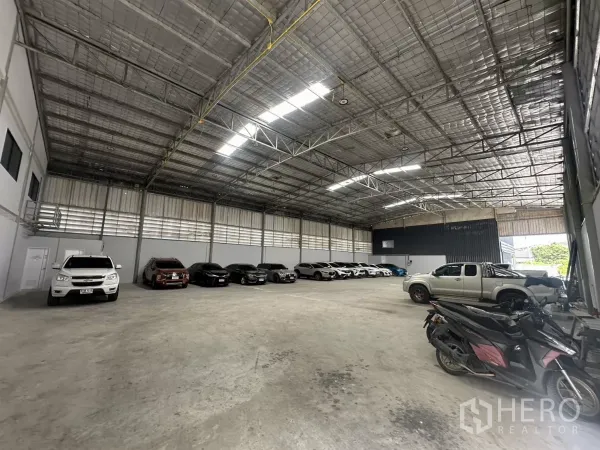 Warehouse for rent in Suan Luang, Bangkok - Spacious warehouse hall showing ventilated louvres, roll-up doors, and parked cars on both sides.
