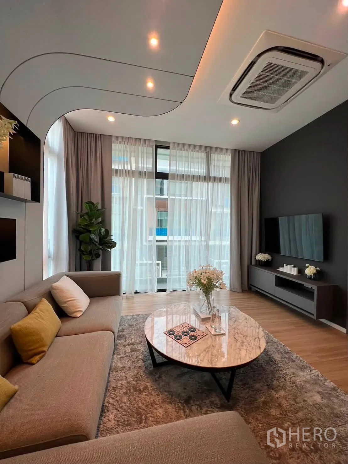 Townhouse for rent in Saphan Sung, Bangkok - Living room with L-shaped sofa, marble coffee table, and tall curtains.