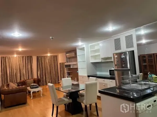 公寓 出租或出售在Watthana, Bangkok - 客厅、餐区与白色厨房一体化，黑色台面、餐桌及不锈钢冰箱。