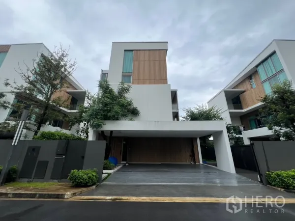 Detached House for rent in Saphan Sung, Bangkok - Front elevation of a modern three-storey detached house with carport and wood accents on a cloudy day.