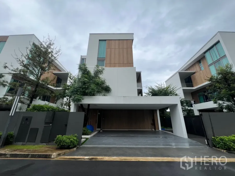 Detached House for rent in Saphan Sung, Bangkok - Front elevation of a modern three-storey detached house with carport and wood accents on a cloudy day.