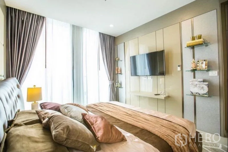 Condominium for rent in Pathum Wan, Bangkok - Master bedroom feature wall with mounted TV, shelves and tall curtains.