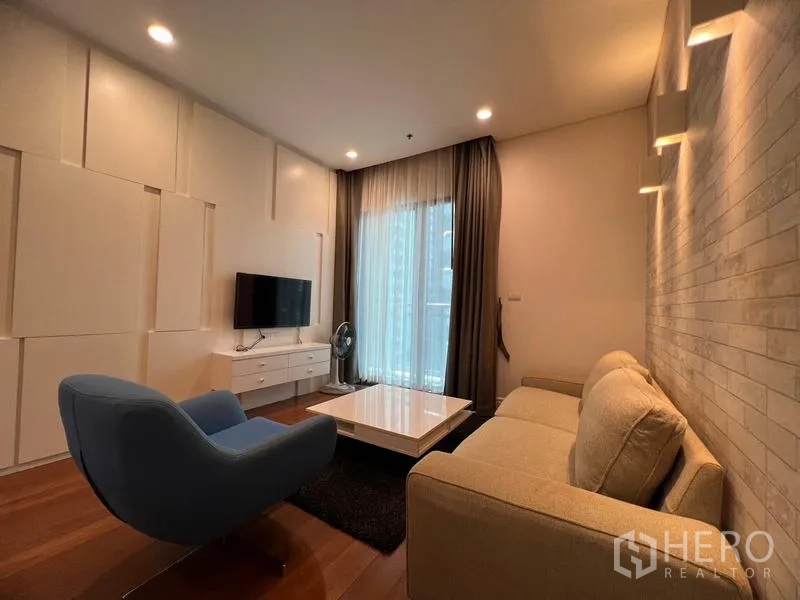 Condominium for rent in Khlong Toei, Bangkok - Cozy living room with sofa, armchair, wall-mounted TV and sliding door to the balcony.