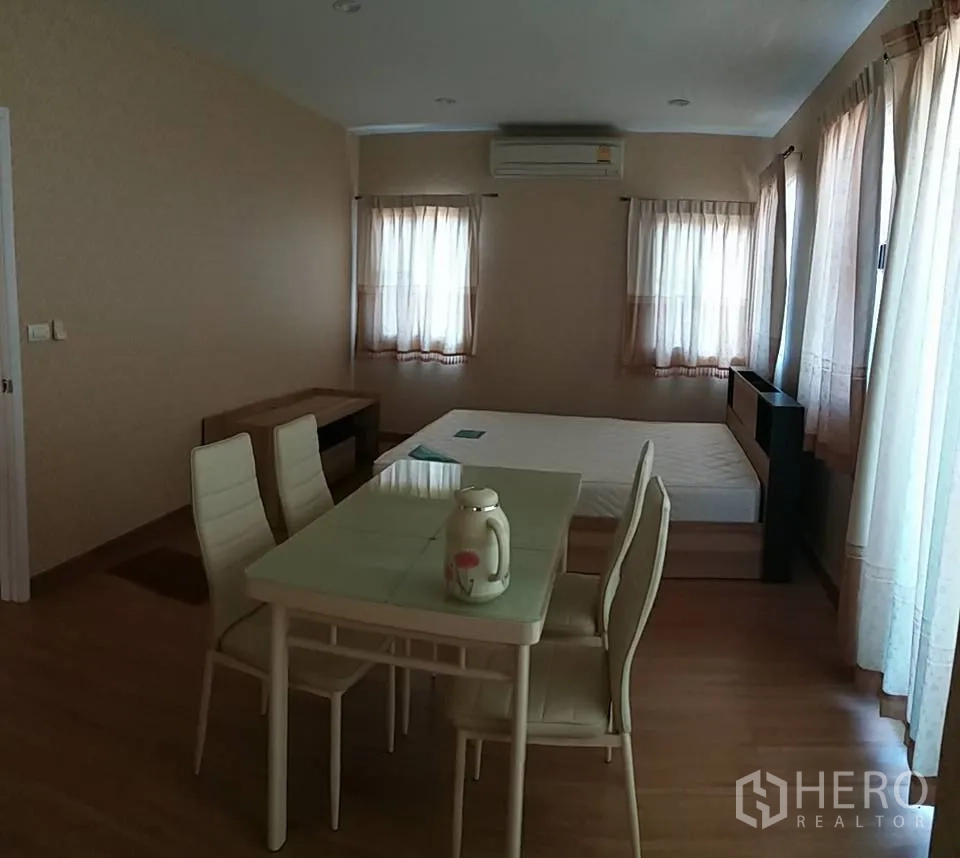 独立式住宅 出租在Pathum Thani - 主卧套房视角，带小餐桌、木地板和多扇窗户