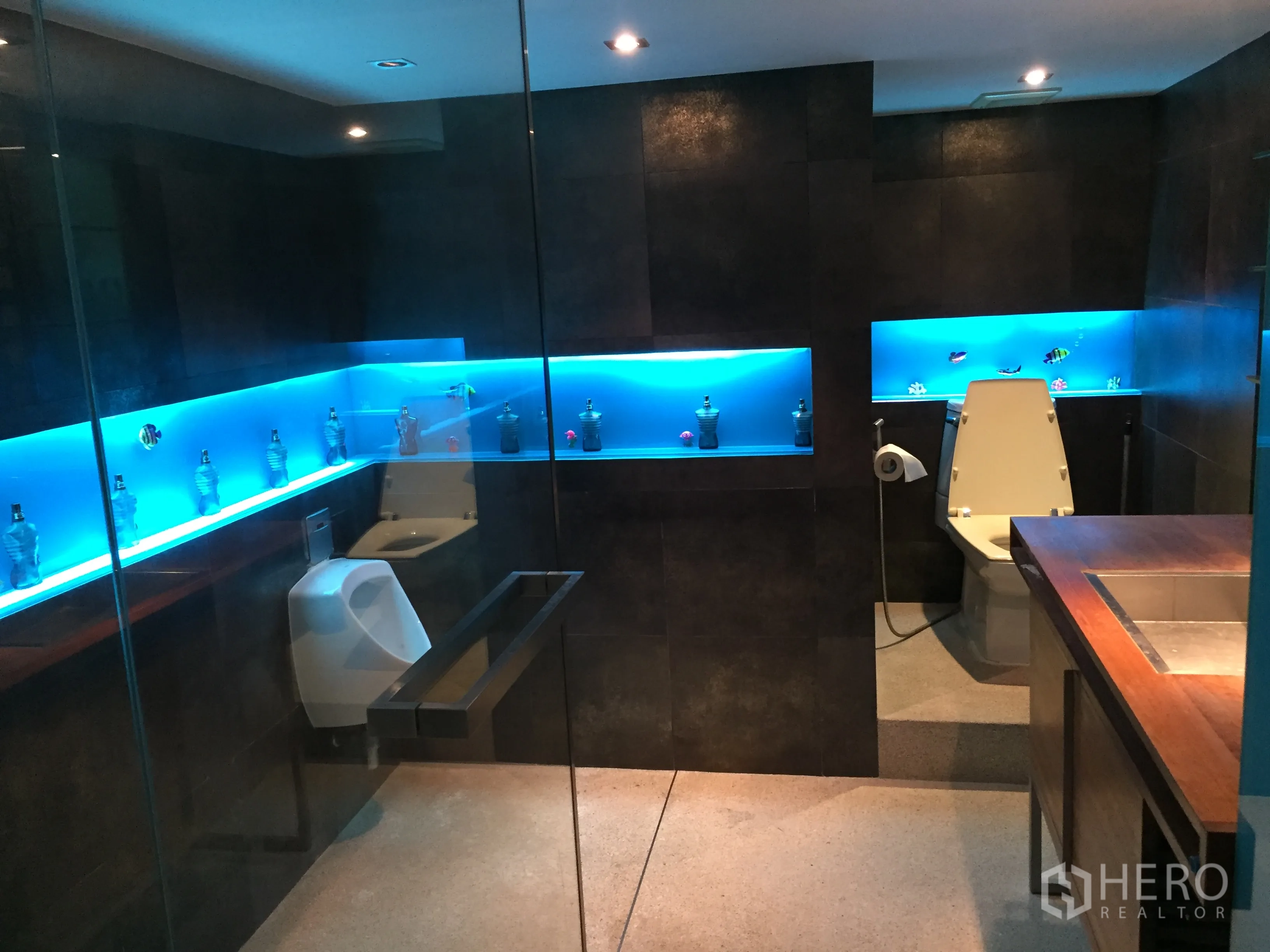 Condominium for rent in Khlong Toei, Bangkok - Modern bathroom with dark tiles, glass partition and blue backlit display niches.