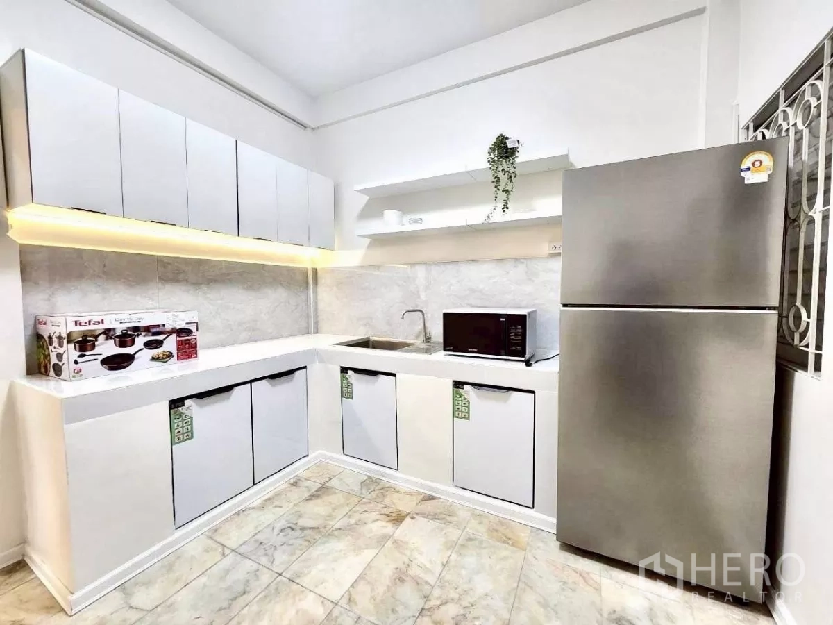 Townhouse for rent in Huai Khwang, Bangkok - Bright Western kitchen with L-shaped cabinets, fridge, microwave and under-cabinet lighting.
