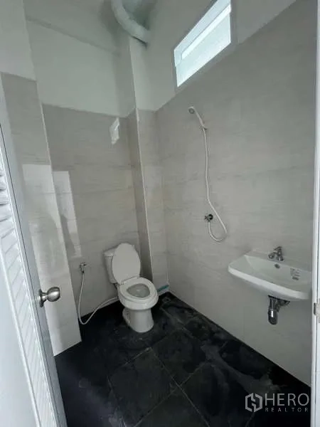 Shophouse for rent in Watthana, Bangkok - Bright bathroom with shower, toilet, and wall-mounted sink on dark tile floor.