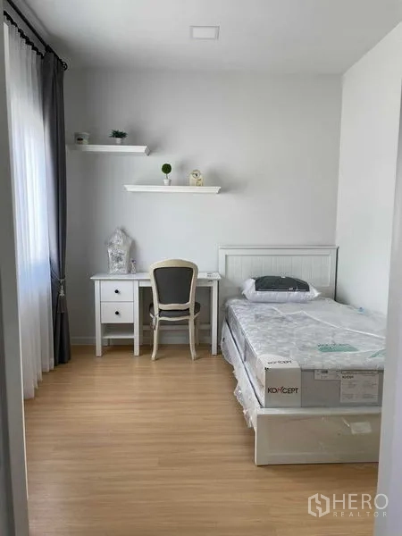 Townhouse for rent in Samut Prakan - Secondary bedroom with single bed, study desk, wall shelves and bright window.