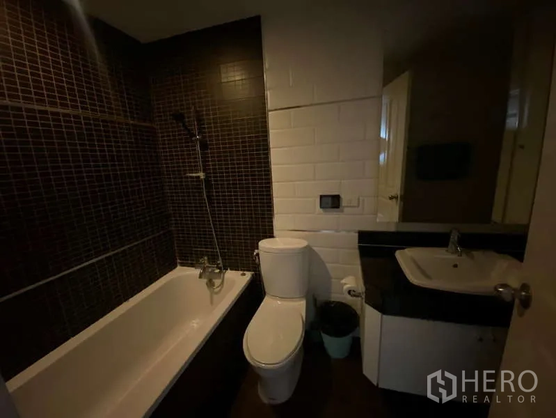 Condominium for rent in Khlong Toei, Bangkok - Moody bathroom with bathtub and shower combo, toilet and vanity with sink.