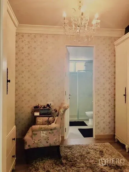 Townhouse for rent or sale in Bangkok - Dressing area with chandelier, floral wallpaper and access to a bathroom with glass shower.