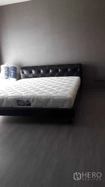 Townhouse for rent - Minimal bedroom with a dark tufted bed frame and new mattress against gray walls and flooring.