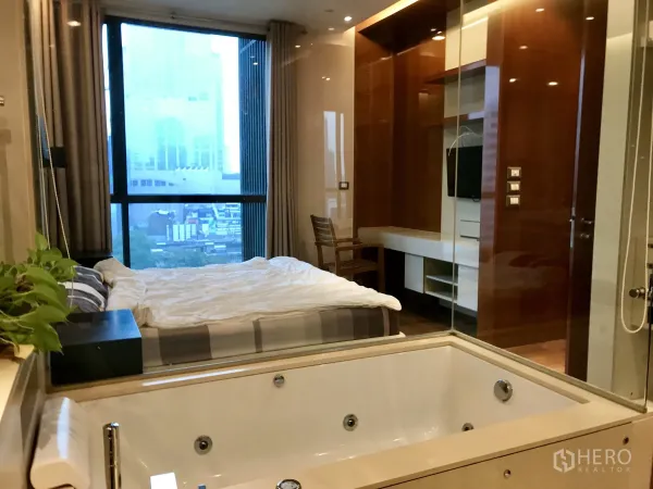 公寓 出租或出售在Khlong Toei, Bangkok - 卧室配落地窗观景、内置电视墙，玻璃隔断旁设按摩浴缸。