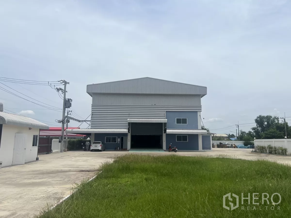 Factory for sale in Lat Lum Kaeo, Pathum Thani - Wide frontage of the factory behind a lawn, showing driveway and twin roller doors.