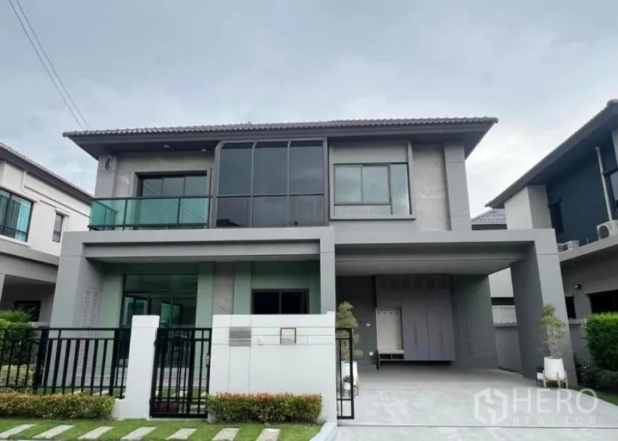Detached House for sale in Bang Kruai, Nonthaburi - Front elevation of the two-storey house with black metal fence, landscaped lawn and covered parking.
