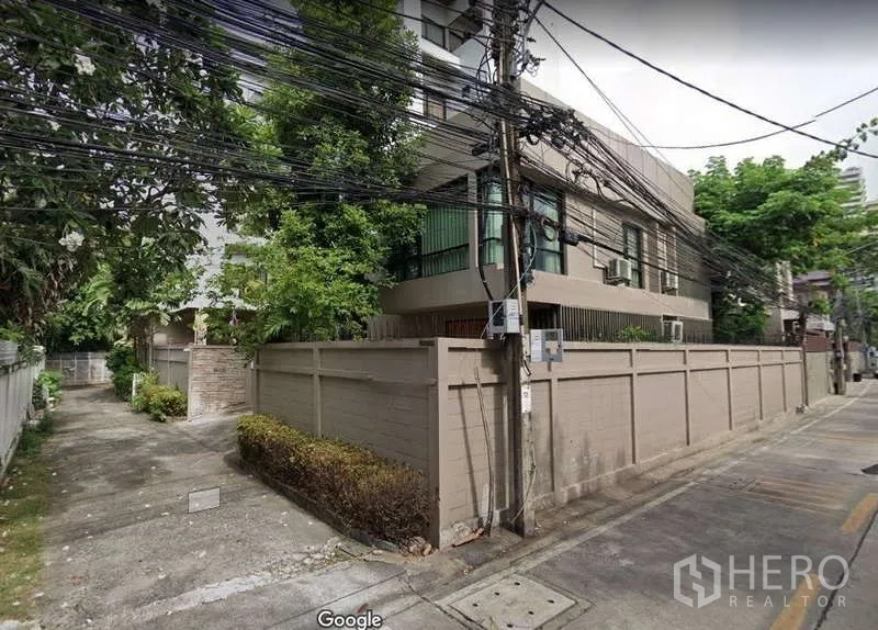 独立式住宅 出租 - 曼谷安静小巷中的带围墙独栋住宅转角外观，绿树环绕。