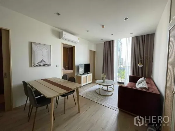 公寓 出租在Watthana, Bangkok - 瓦他那区公寓的现代客厅，落地窗、电视柜与餐桌，可见城市景观。