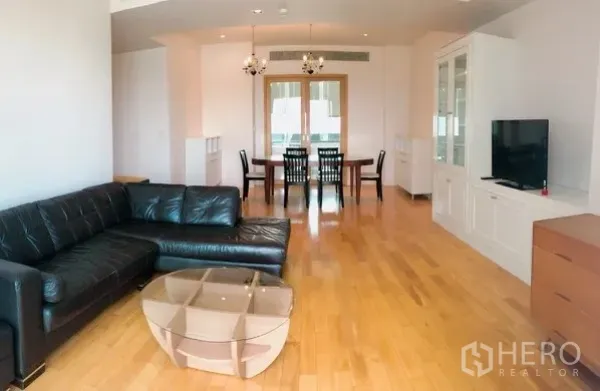 Condominium for rent or sale in Khlong Toei, Bangkok - Bright living and dining area with black leather sectional, chandeliers, hardwood floors and built‑in TV cabinet in a Sukhumvit Asok condo.