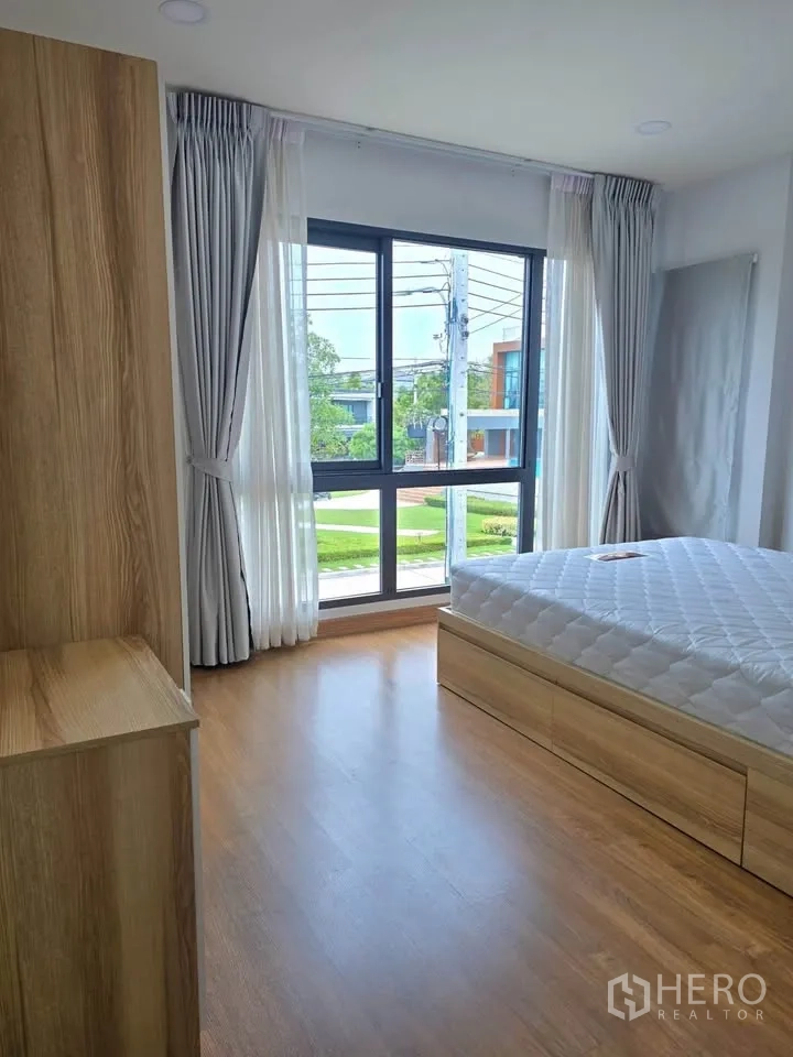 Detached House for rent or sale in Bang Phli, Samut Prakan - Corner bedroom with large windows, wood floors, and a platform bed.