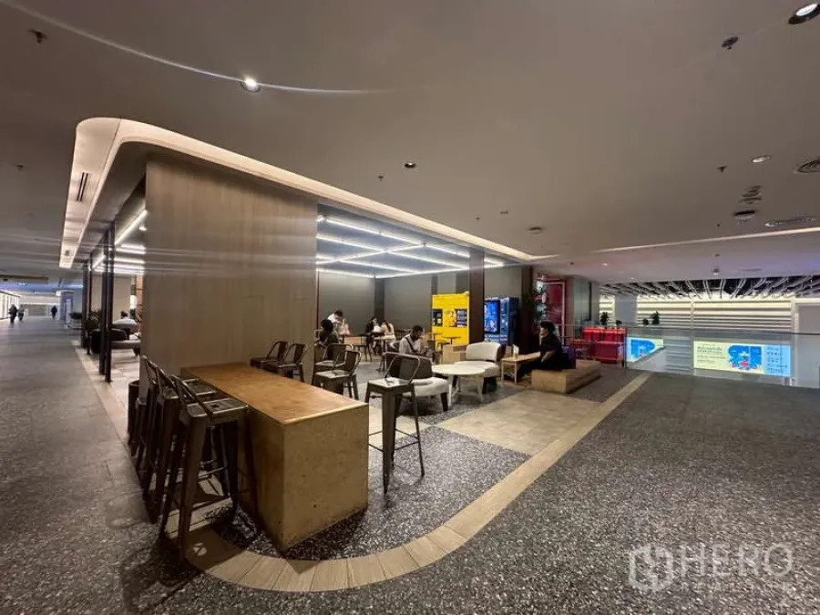 Retail Space for rent - Modern indoor retail lounge with bar-height table, stools, LED grid ceiling lights, vending machines and polished floors in a shopping complex.