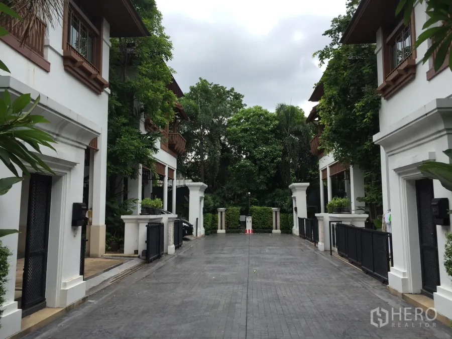 Detached House for rent in Yan Nawa, Bangkok - Gated driveway between white villas with lush trees in a quiet compound.