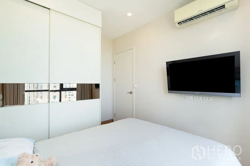 公寓 出租在Watthana, Bangkok - 卧室配推拉衣柜、壁挂电视与空调，瓦他那区公寓内景。