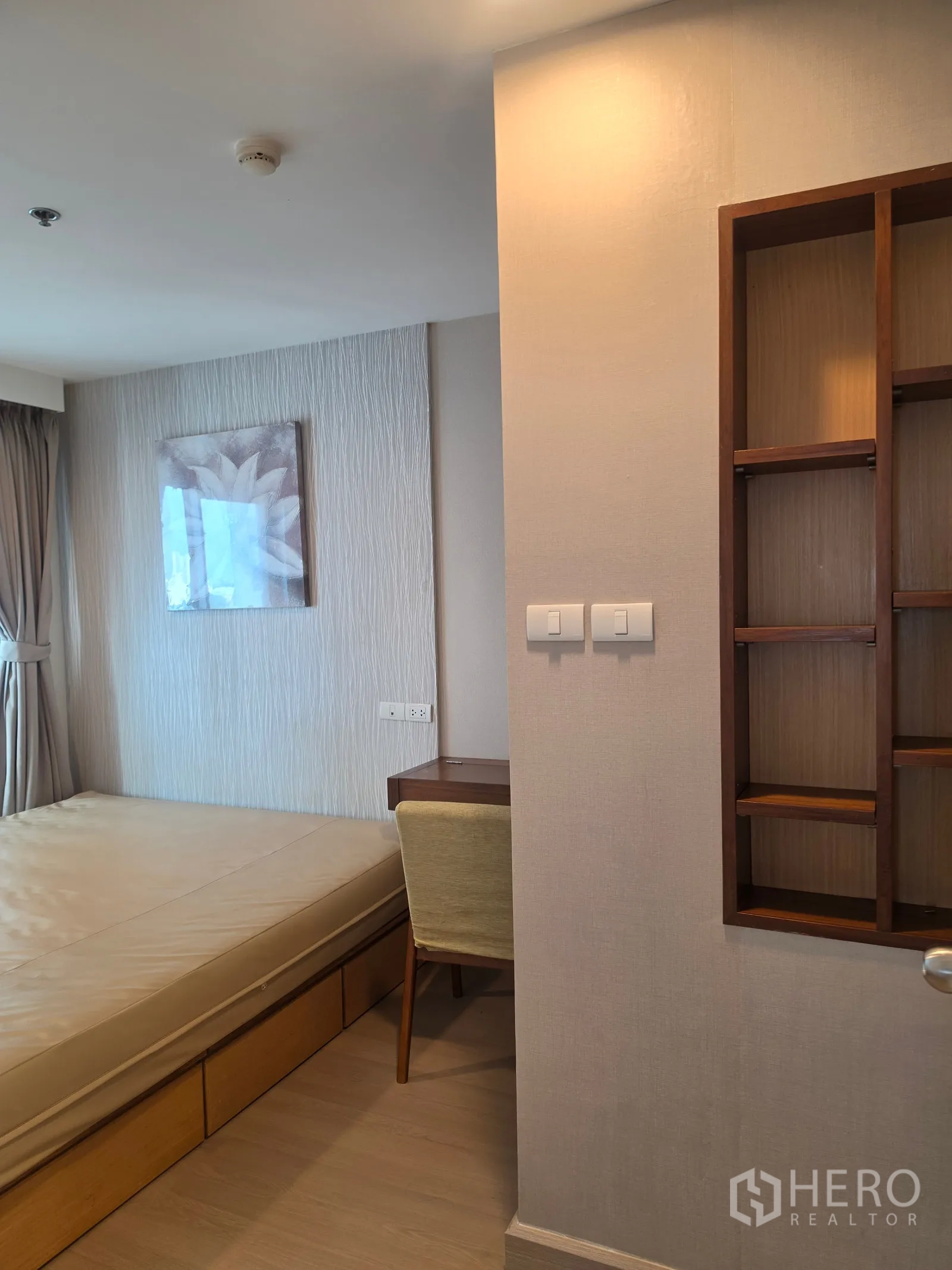 Condominium for rent in Huai Khwang, Bangkok - Bedroom angle showing platform bed, wall shelves, and window with curtains.