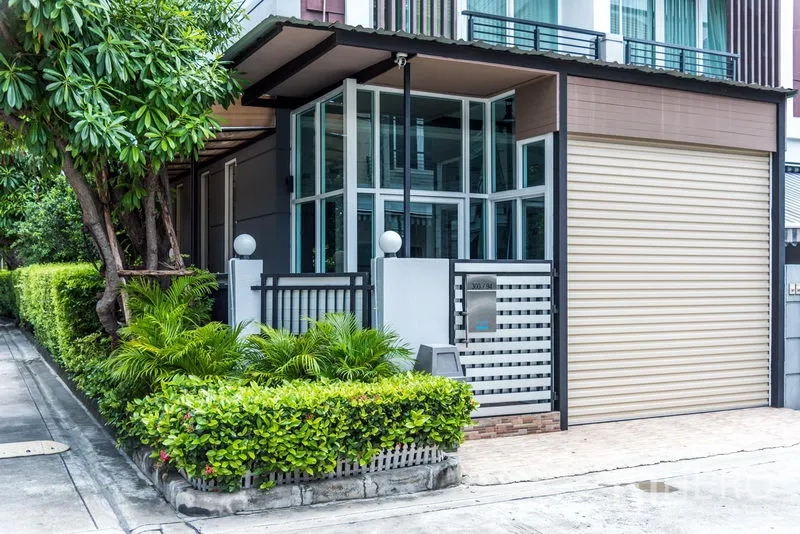 联排别墅 出售在Wang Thonglang, Bangkok - 现代联排别墅外观，转角落地窗、庭院绿篱与大门。