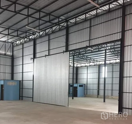 Warehouse for rent in Khan Na Yao, Bangkok - Warehouse hall with sliding metal partition separating two bays under a high ceiling.