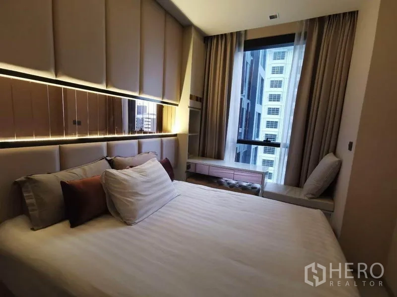 公寓 出租或出售在Ratchathewi, Bangkok - 卧室配软包床头与大窗，享城市景观与暖色灯光，位于拉差贴威公寓内。