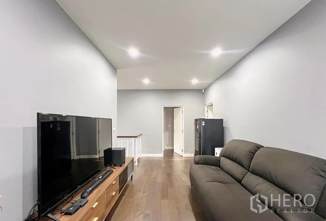 Detached House for rent or sale in Lam Luk Ka, Pathum Thani - Upper lounge with TV, sofa and wood floors next to stair landing.