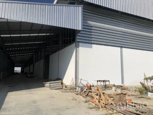 Warehouse for rent in Bang Phli, Samut Prakan - Covered loading bay along the warehouse with wide driveway and stacked construction materials.