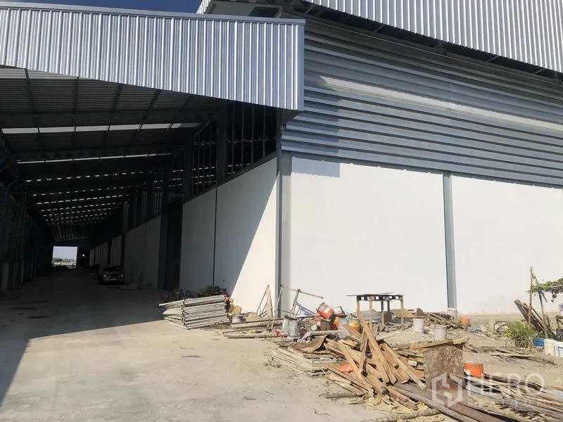 Warehouse for rent in Bang Phli, Samut Prakan - Covered loading bay along the warehouse with wide driveway and stacked construction materials.