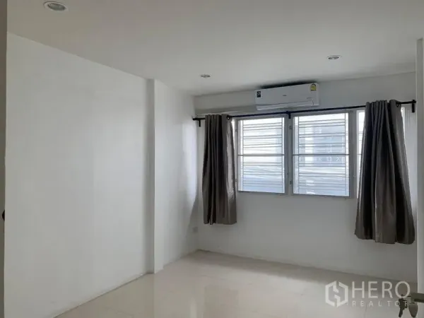 Townhouse for rent in Din Daeng, Bangkok - Airy bedroom with three windows, curtains and a wall-mounted air conditioner.