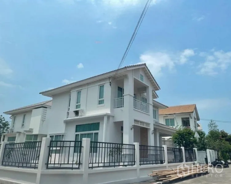 Detached House for sale in Lat Krabang, Bangkok - Two-storey white detached house with small balcony and metal fence on a corner plot under a blue sky.