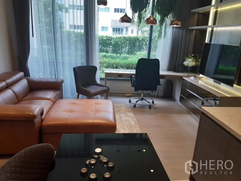 公寓 出租或出售在Watthana, Bangkok - 明亮客厅配皮质沙发、落地窗、花园景观、电视墙与靠窗书桌。