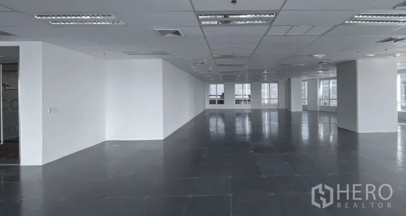 สำนักงาน ให้เช่า - พื้นที่ชั้นสำนักงานกว้างพร้อมเสา ผนังสีขาว เพดานแขวนไฟ และหน้าต่างหลายบานรับแสงธรรมชาติ