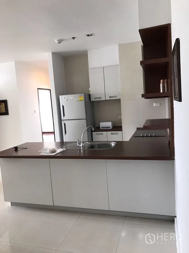 公寓 出租在Watthana, Bangkok - 曼谷瓦塔那区公寓开放式厨房，带岛台、水槽、木质台面、电磁炉与白色橱柜及大冰箱。