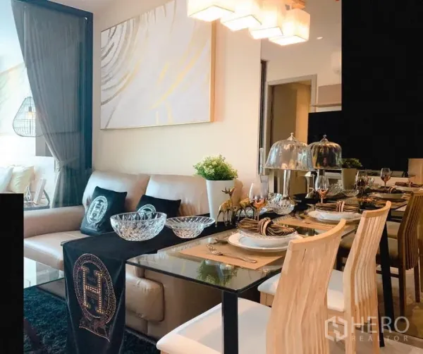 Condominium for rent in Watthana, Bangkok - Open-plan living and dining area with glass table, pendant lights, artwork and a cream sofa in a modern Bangkok condo.