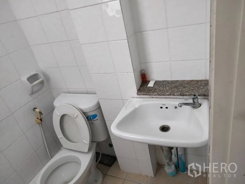 Shophouse for rent - Compact white‑tiled bathroom with toilet and wall‑mounted sink.