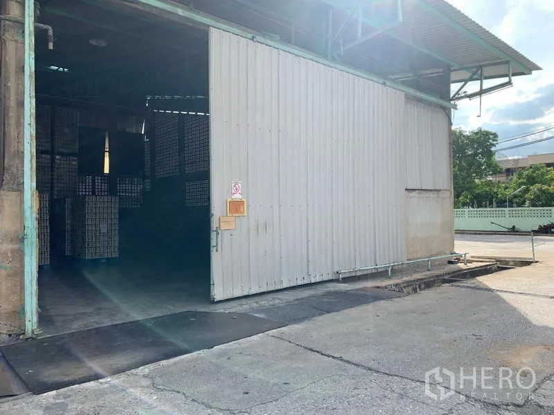 Warehouse for rent in Mueang Pathum Thani, Pathum Thani - Covered loading bay with a large sliding door and driveway access beside the warehouse.