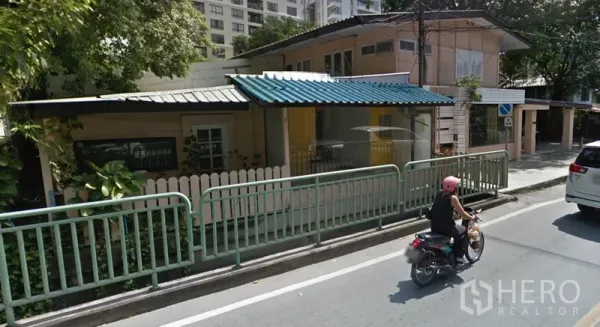 Retail Space for rent in Watthana, Bangkok - Street-facing two-storey retail building with large glass storefront, metal awnings and roadside railings under trees.