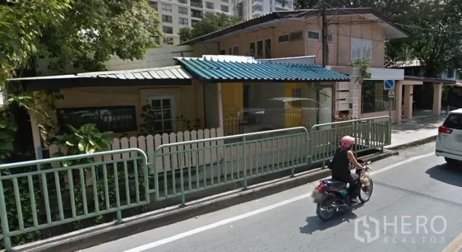 Retail Space for rent in Watthana, Bangkok - Street-facing two-storey retail building with large glass storefront, metal awnings and roadside railings under trees.