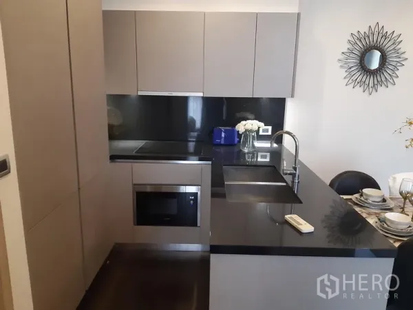 Condominium for rent in Watthana, Bangkok - Compact contemporary kitchen with black countertop and built-in appliances.
