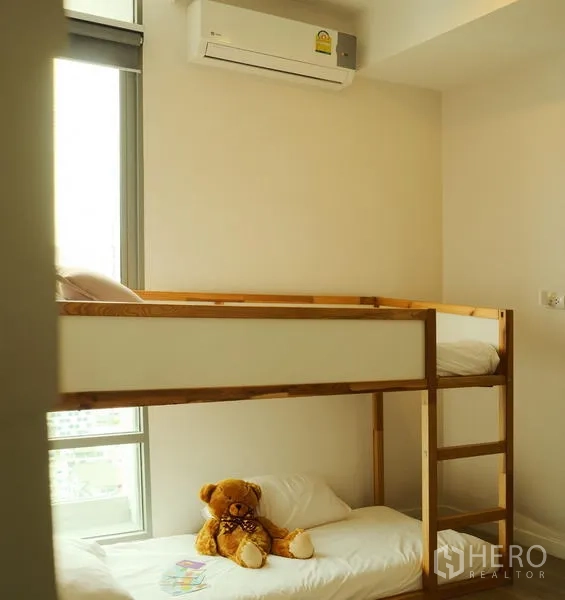 Condominium for rent in Bang Rak, Bangkok - Compact bedroom with wooden bunk bed beside a tall window and wall-mounted AC.