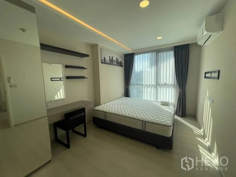 Condominium for rent in Khlong Toei, Bangkok - Primary bedroom with large window, desk and shelves, and a queen mattress.