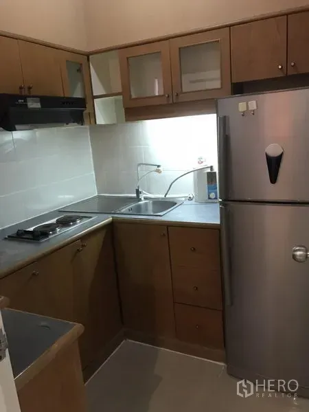 Condominium for rent in Watthana, Bangkok - Compact L-shaped kitchen with wooden cabinets, double sink, hob, hood and stainless refrigerator.
