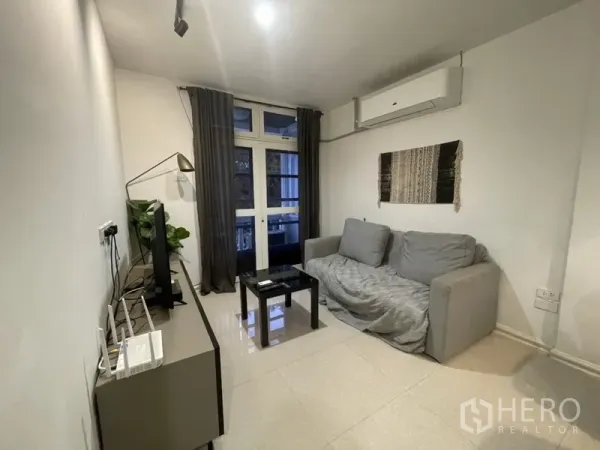 Home Office for rent or sale in Watthana, Bangkok - Cozy living room with sofa, TV console, split-type air conditioner and glass doors to a balcony.