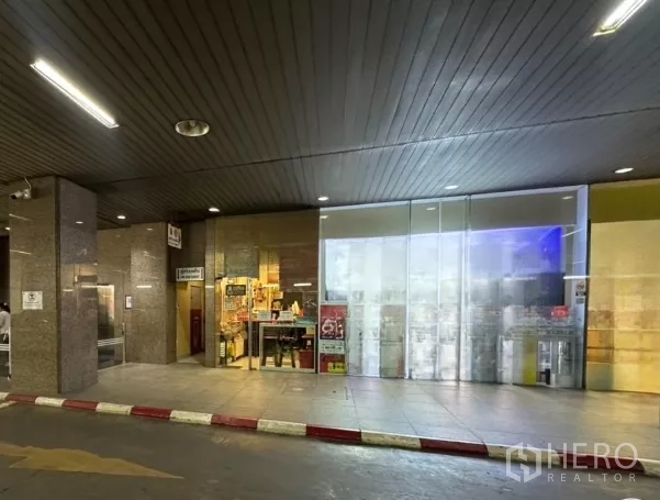 Retail Space for rent - Glass-fronted shop unit beneath a covered walkway with polished stone columns and exterior lighting.
