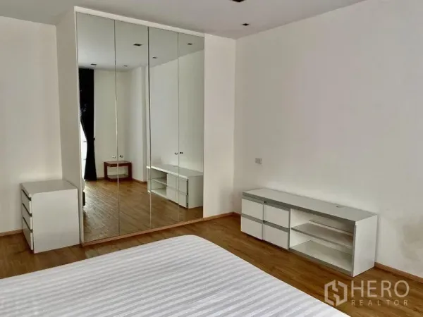 Condominium for rent in Khlong Toei, Bangkok - Bedroom with mirrored built-in wardrobes and white drawer cabinets on wooden floors.